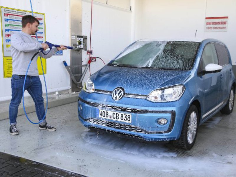  Ein blauer VW UP wird in der Waschanlage von einem Mann geputzt. 